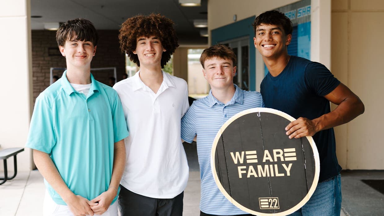 Four students smiling with a We Are Family sign