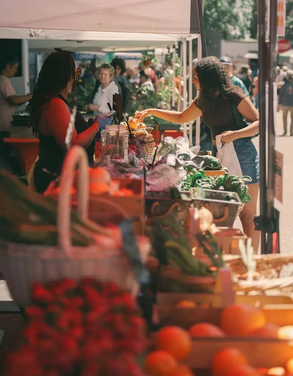 Neighbors talking over a produce stand at an outdoor market