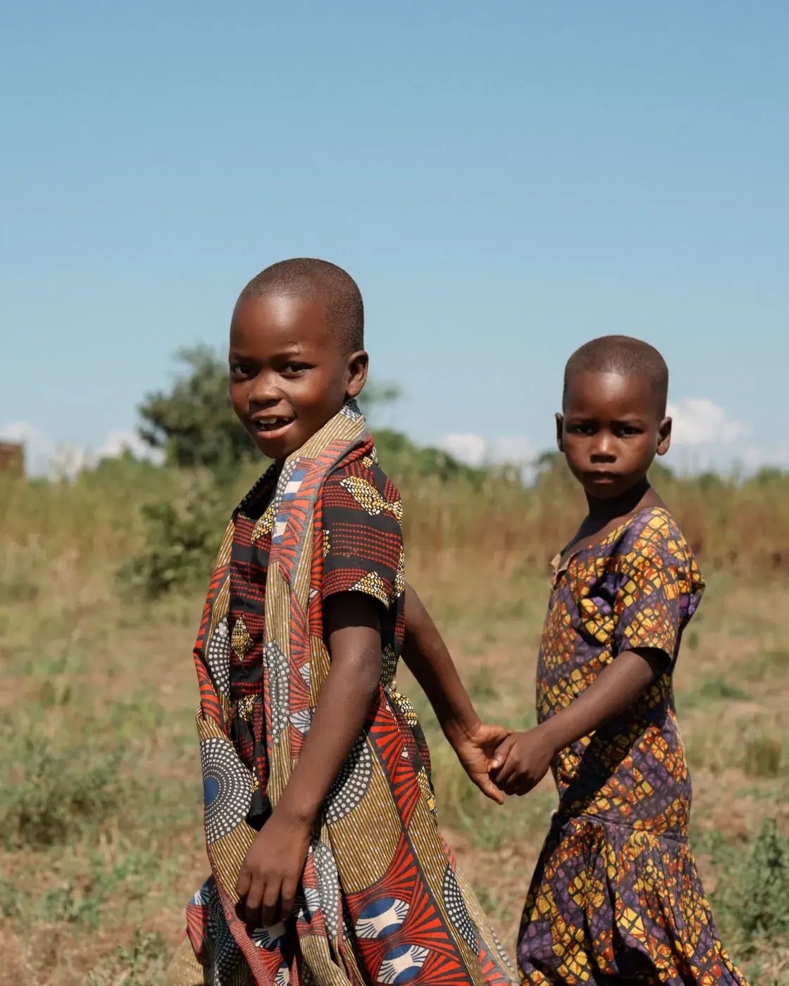 Two children holding hands in a field, one looking back at the camera